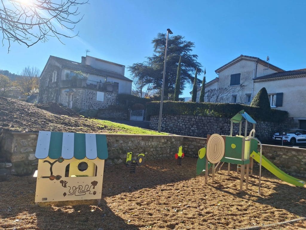 Aire de jeux pour enfants avec toboggan, maison miniature et jeux à ressort dans un quartier résidentiel ensoleillé.