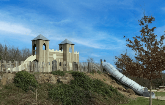 Aire de jeux Ludoparc en forme de château médiéval avec toboggans, intégrée dans le relief naturel à Pinel-Hauterive.