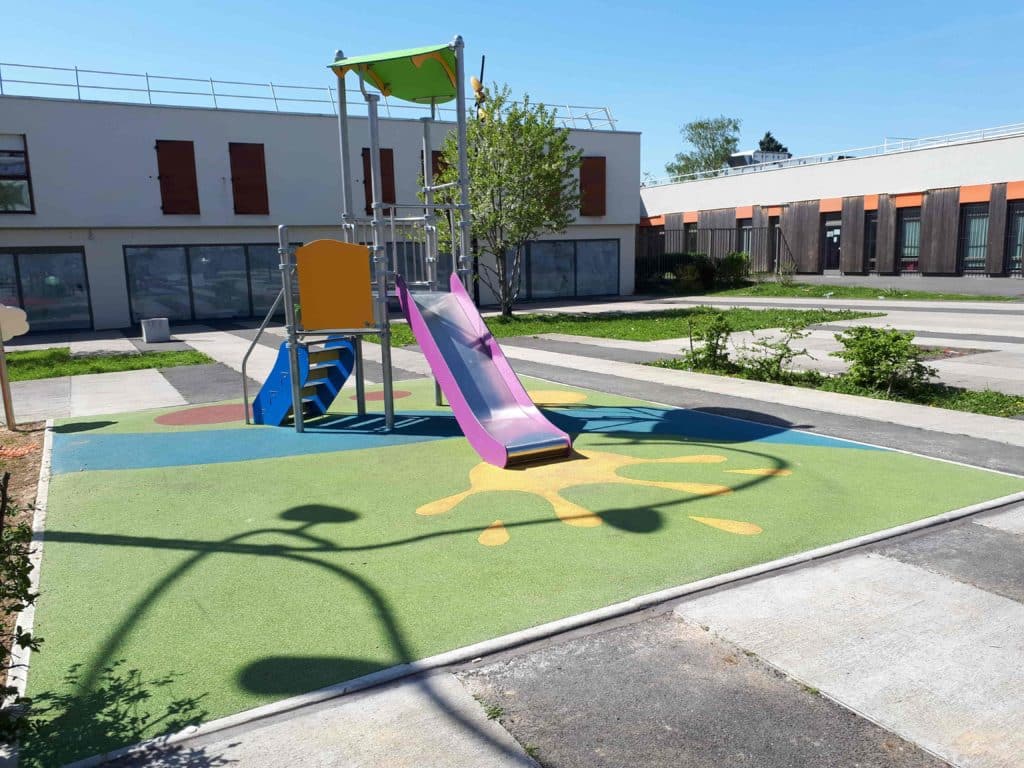 Aire de jeux colorée avec toboggan et sol souple dans une cour oasis.
