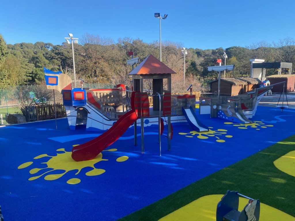 Aire de jeux thématique pour enfants en forme de bateau pirate, avec toboggans rouges et bleus, filets et passerelles.