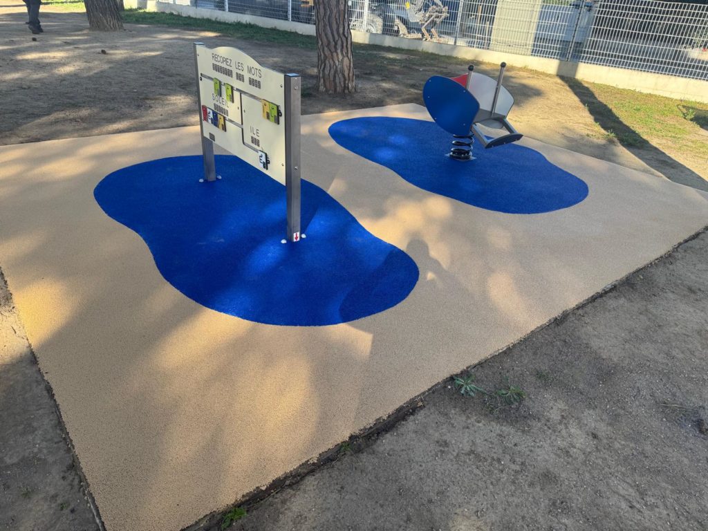 Aire de jeux pour enfants avec panneau éducatif et jeu à ressort installé sur sol amortissant coloré.