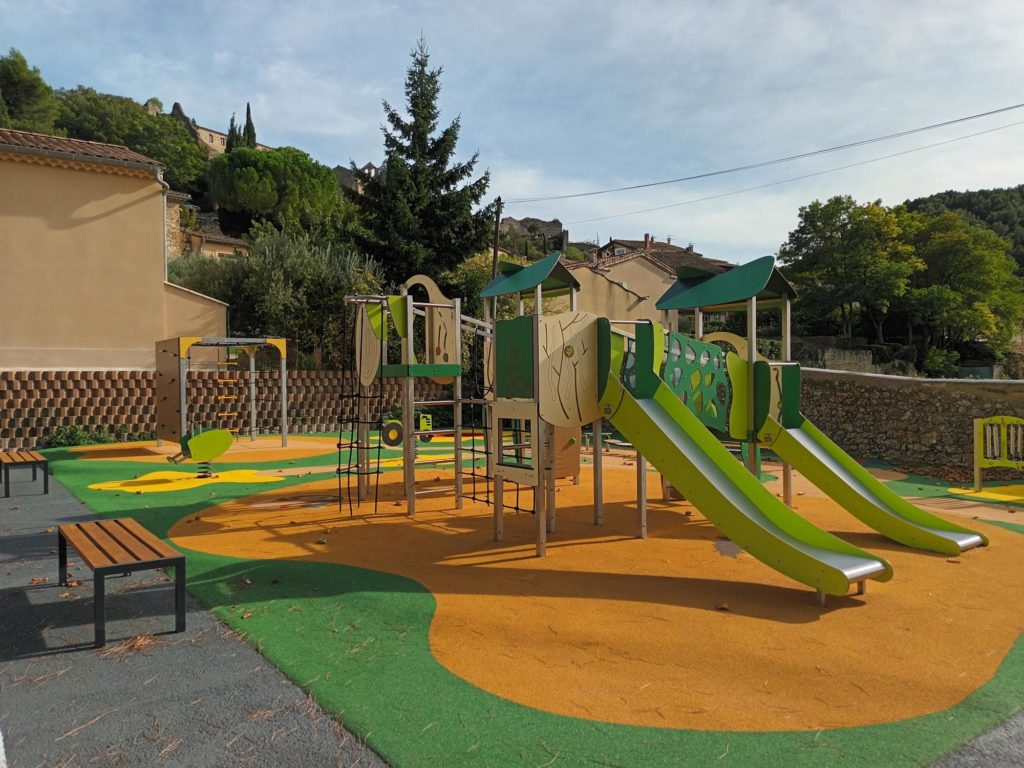 Aire de jeux extérieure avec deux toboggans verts, structures à grimper et bancs pour les familles.