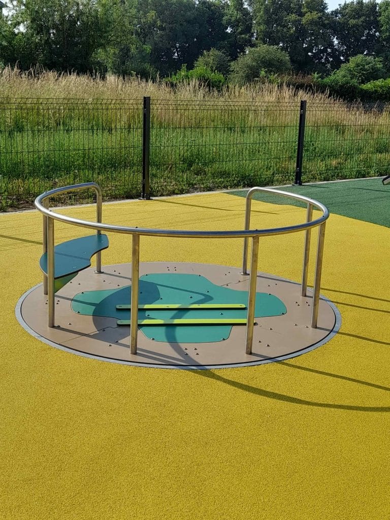 Tourniquet PMR sur une aire de jeux Ludoparc avec sol souple jaune et vert, conçu pour accueillir tous les enfants, y compris ceux en fauteuil roulant.