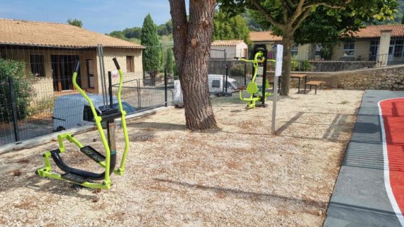 Texte alternatif : Zone fitness extérieure avec plusieurs appareils de musculation verts dans une cour d'école provençale arborée