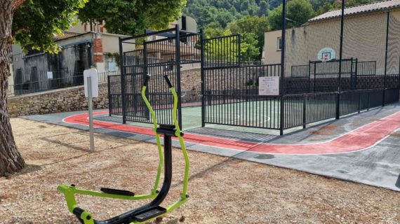 Appareil de fitness extérieur vert avec terrain multisports et piste running en arrière-plan dans une aire de loisirs