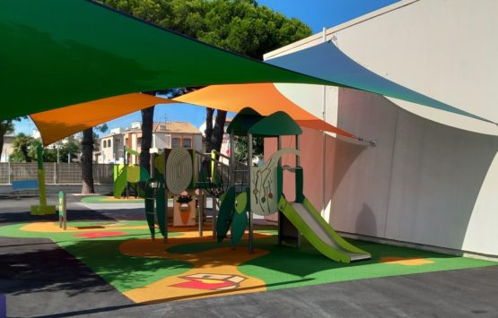 Aire de jeux ombragée avec toiles tendues colorées et structure ludique verte et orange installée dans une cour d’école.