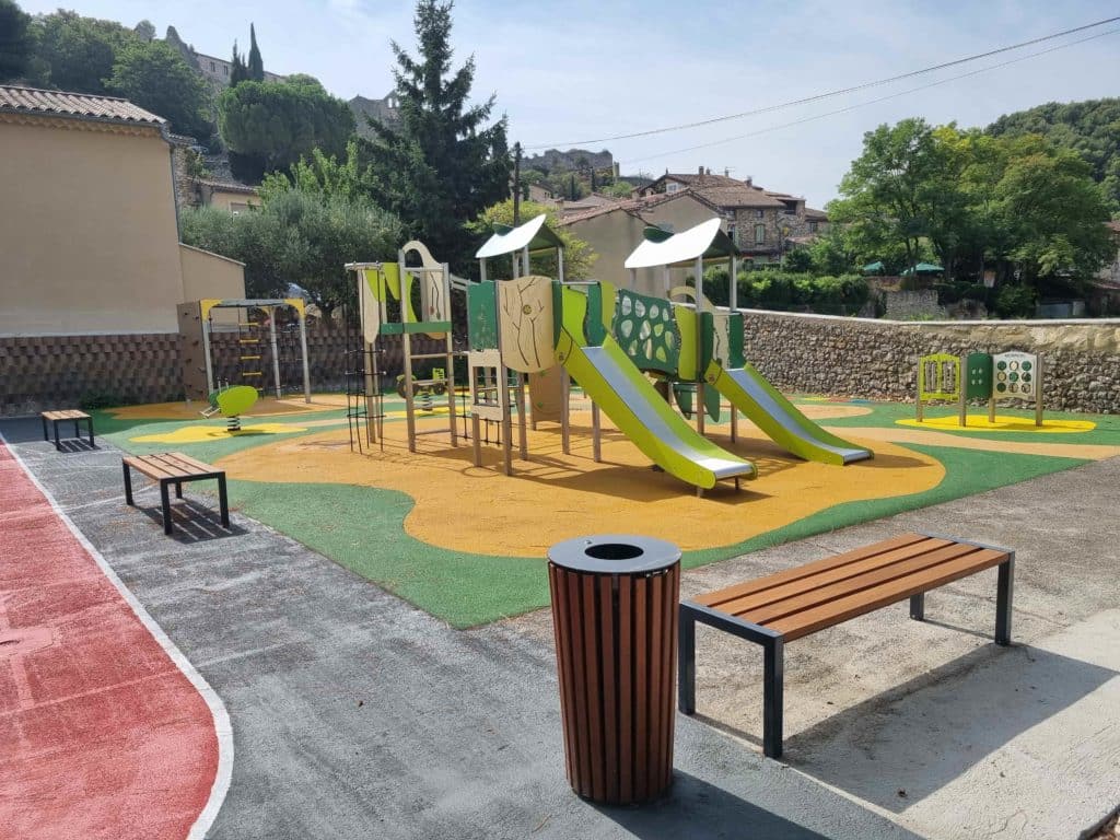 Structure de jeux pour enfants avec toboggans verts et jaunes, banc urbain et poubelle sur aire de jeux colorée