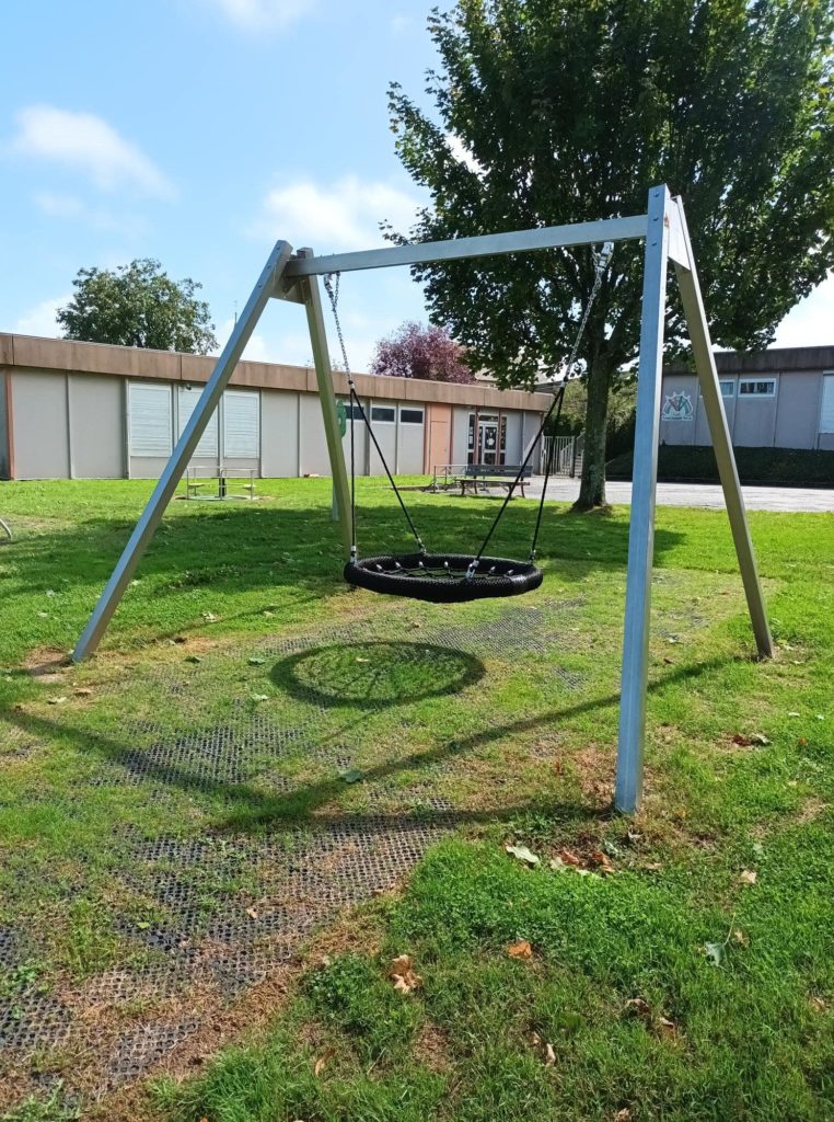 Balançoire nid d'oiseau installée sur une aire de jeux en pelouse équipée de dalles amortissantes pour sécuriser la zone.