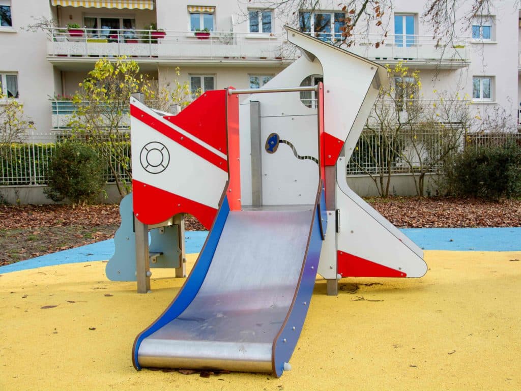 Petite structure de jeux en forme de bateau rouge et blanc avec toboggan sur sol souple EPDM jaune