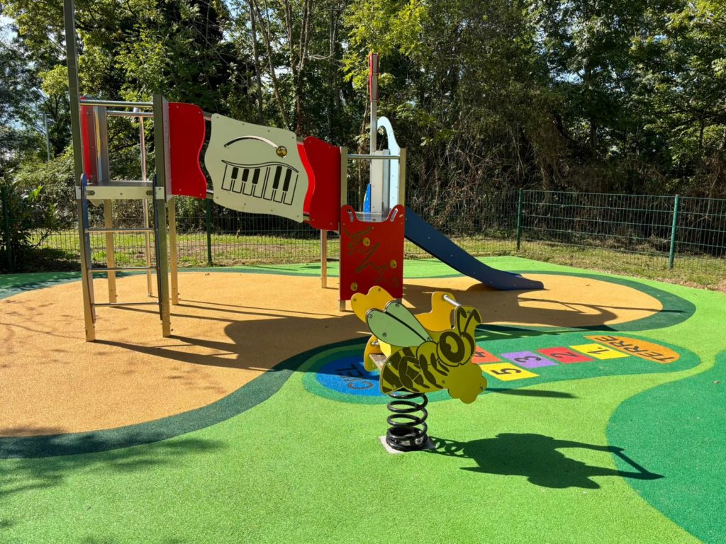 Structure de jeu musicale avec toboggan et jeu ressort abeille avec sol souple coloré dans une aire de jeux extérieure.