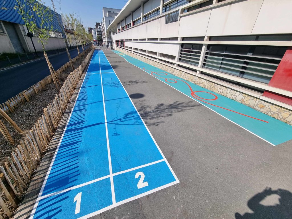 Piste athlétisme bleue numérotée et parcours motricité turquoise sur le parvis d'une école