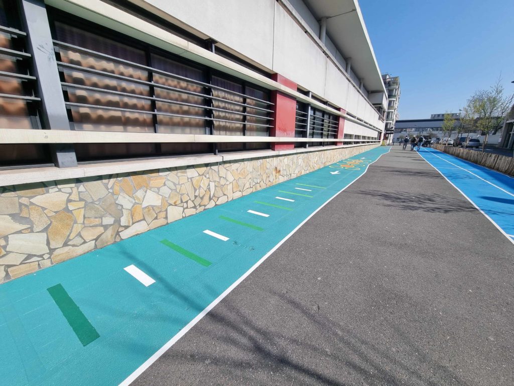 Parcours motricité turquoise marquages rythmiques blancs et verts le long d'un bâtiment scolaire
