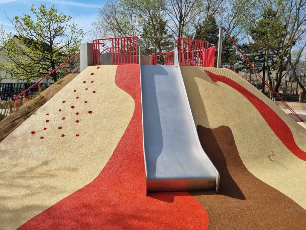 Zoom sur un toboggan sur butte et des prises d'escalade rouges.