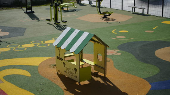 Jeux pour enfants maisonnette sur sol souple en EPDM avec équipements de fitness en arrière plan.